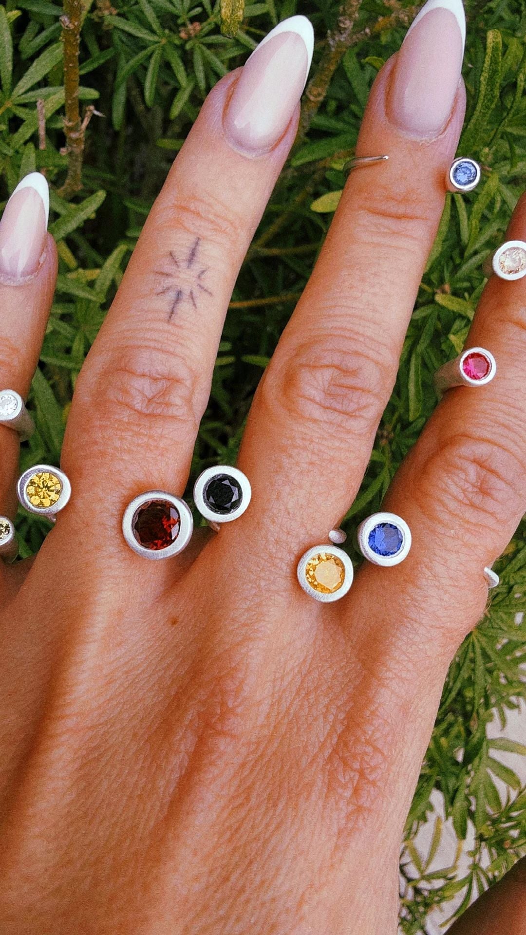 A hand wearing several handmade fine silver rings set with coloured stones width=