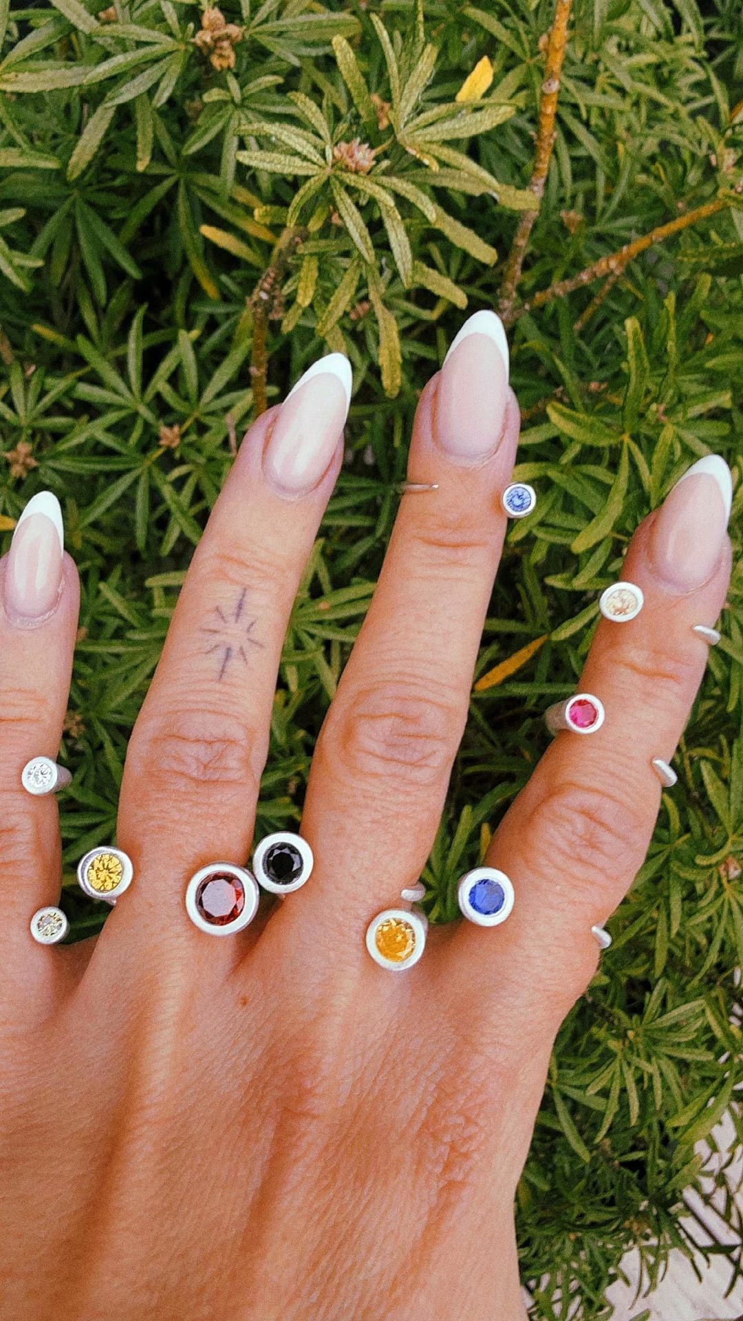 A hand wearing several slim handmade silver stacking rings set with coloured stones