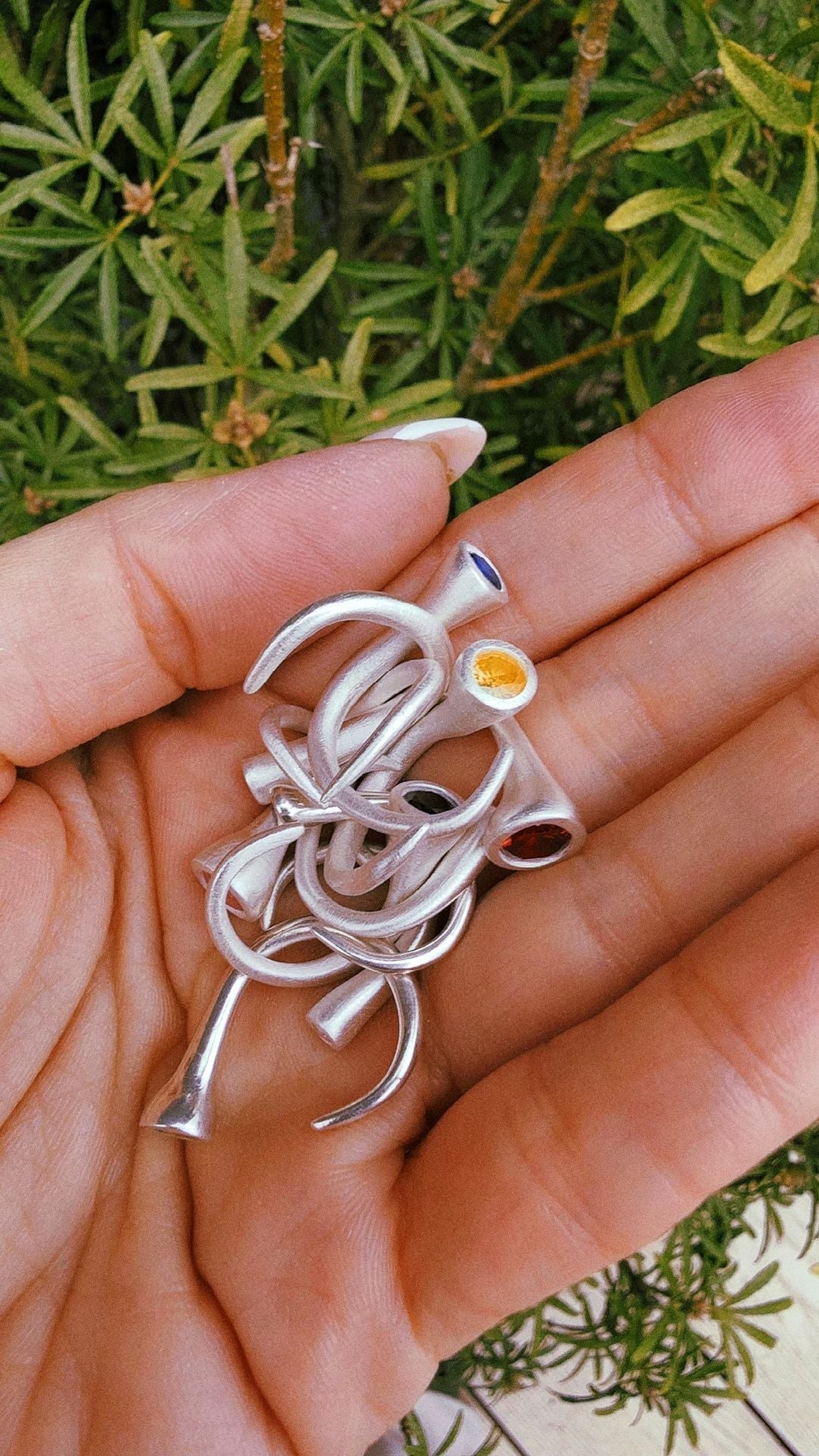 A handful of handmade fine silver pieces set with coloured gemstones, resting in an open palm