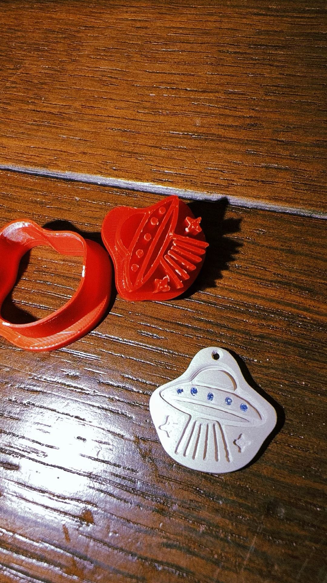 Red silicone mould beside a pressed silver clay pendant set with small blue stones, drying on a wooden table
